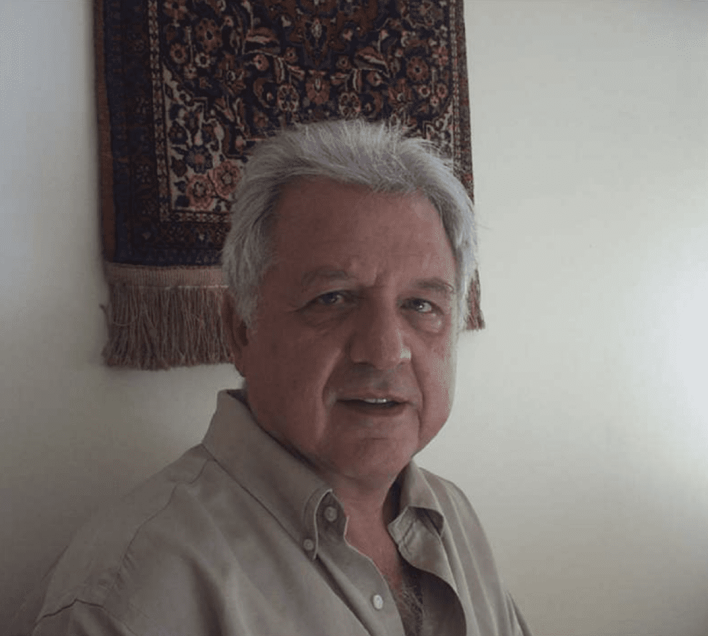 Foto de busto do professor Constantino Tsallis, um senhor branco, de cabelos brancos e camisa bege.