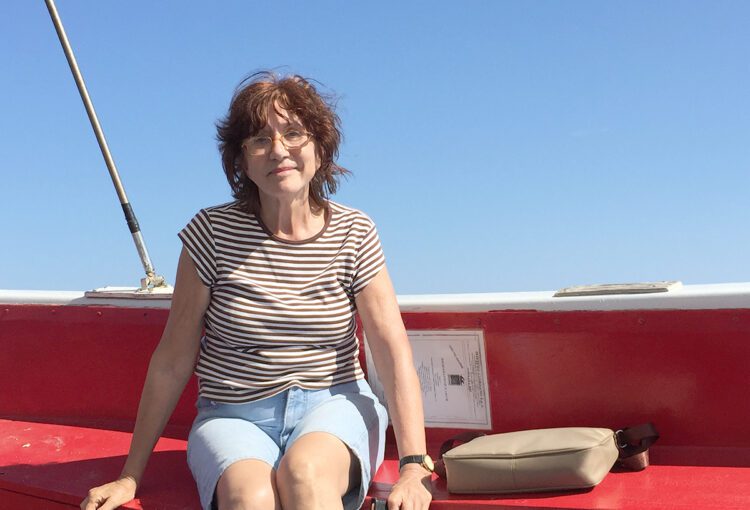 Professora Alinka sentada em uma embarcação, em um dia de sol.